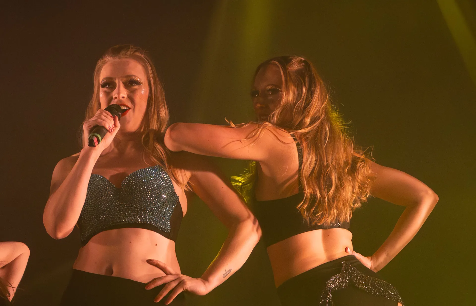 Två showartister sjunger och uppträder i duo på scen med tydlig scennärvaro och publikfokus.