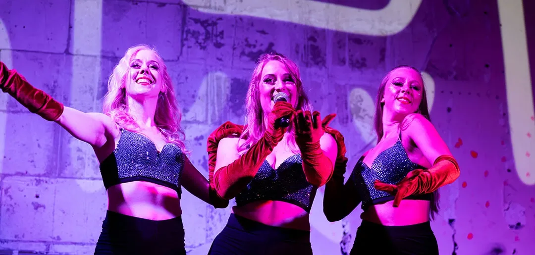 Showartister genomför ett sceniskt gruppnummer med tydlig koreografi och scenljus.