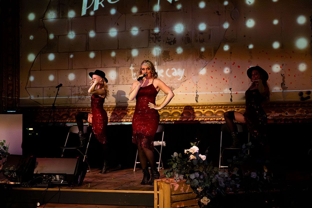 Tre artister från Femme Fusion uppträder på scen i röda paljettklänningar under en show med sång och dans.